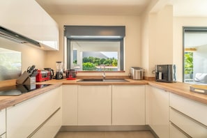 Une cuisine moderne dotée d’un îlot central, d’un four encastré et d’une fenêtre donnant sur un espace verdoyant.