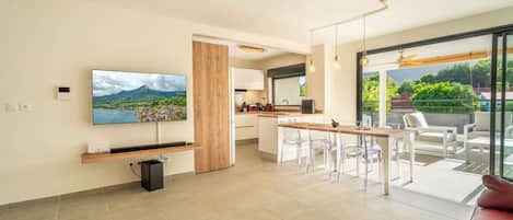 Un espacio habitable moderno con televisor, comedor y balcón con mobiliario exterior.