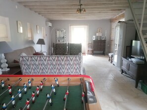 A room with a foosball table, a sofa, a lamp, a mirror, and a television. - Air Conditionned house:  quiet, Greenery & kindness with large pool and garden (Châteauneuf-sur-Charente)