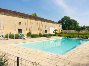 A swimming pool with a tiled deck, a building with arched windows, and a stone wall in the background. - Air Conditionned house:  quiet, Greenery & kindness with large pool and garden (Châteauneuf-sur-Charente)