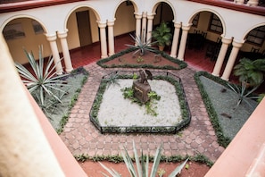 Un patio con una estatua central, rodeado por un camino de ladrillo y plantas.
