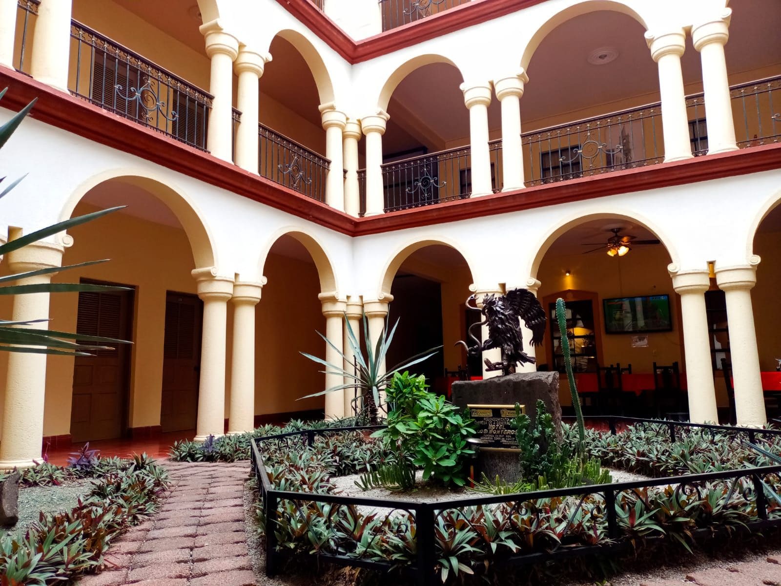 A courtyard with a central fountain, surrounded by arches and columns, and a statue of an eagle.
