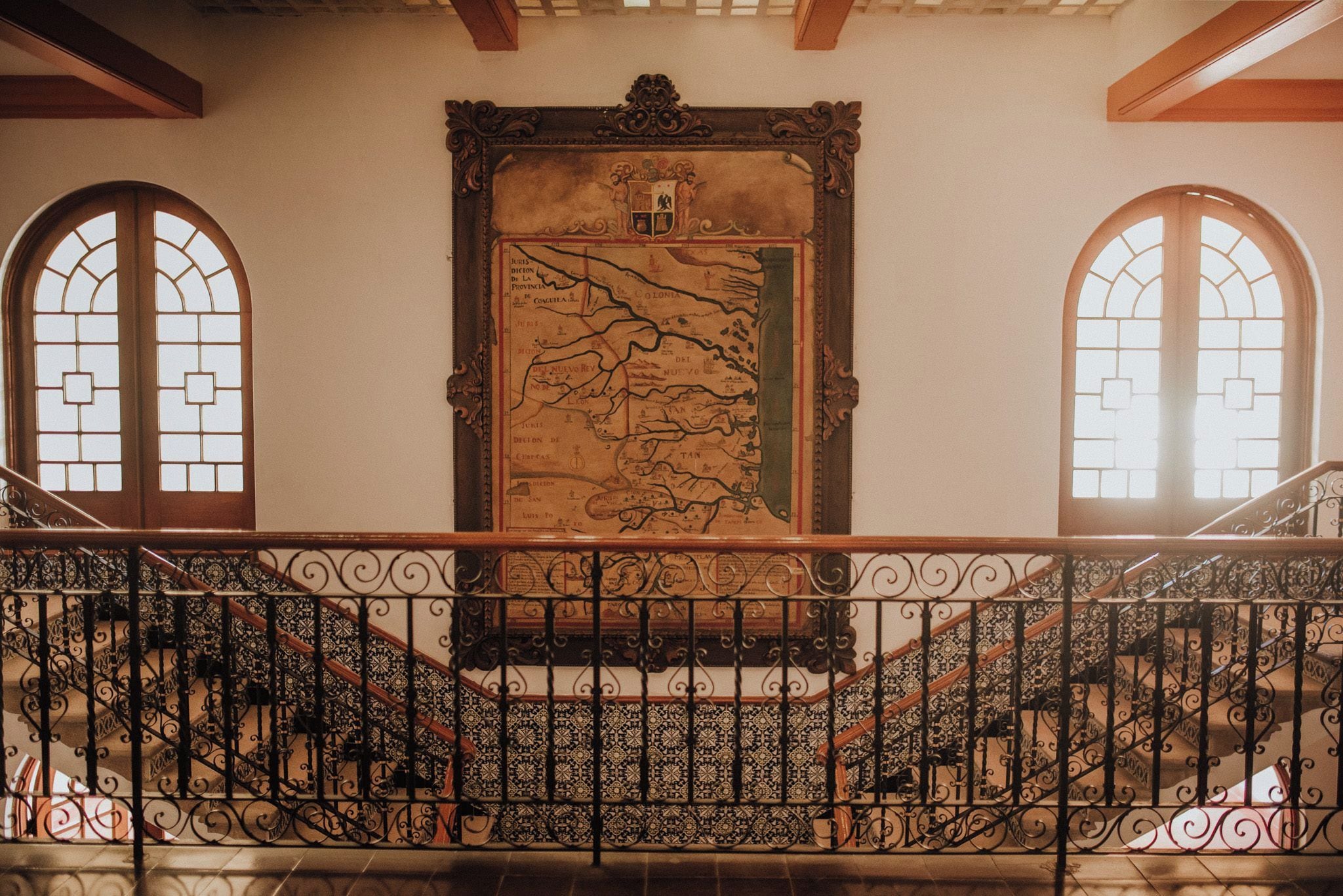 A staircase with ornate iron railings leading to a landing with a large map mural.