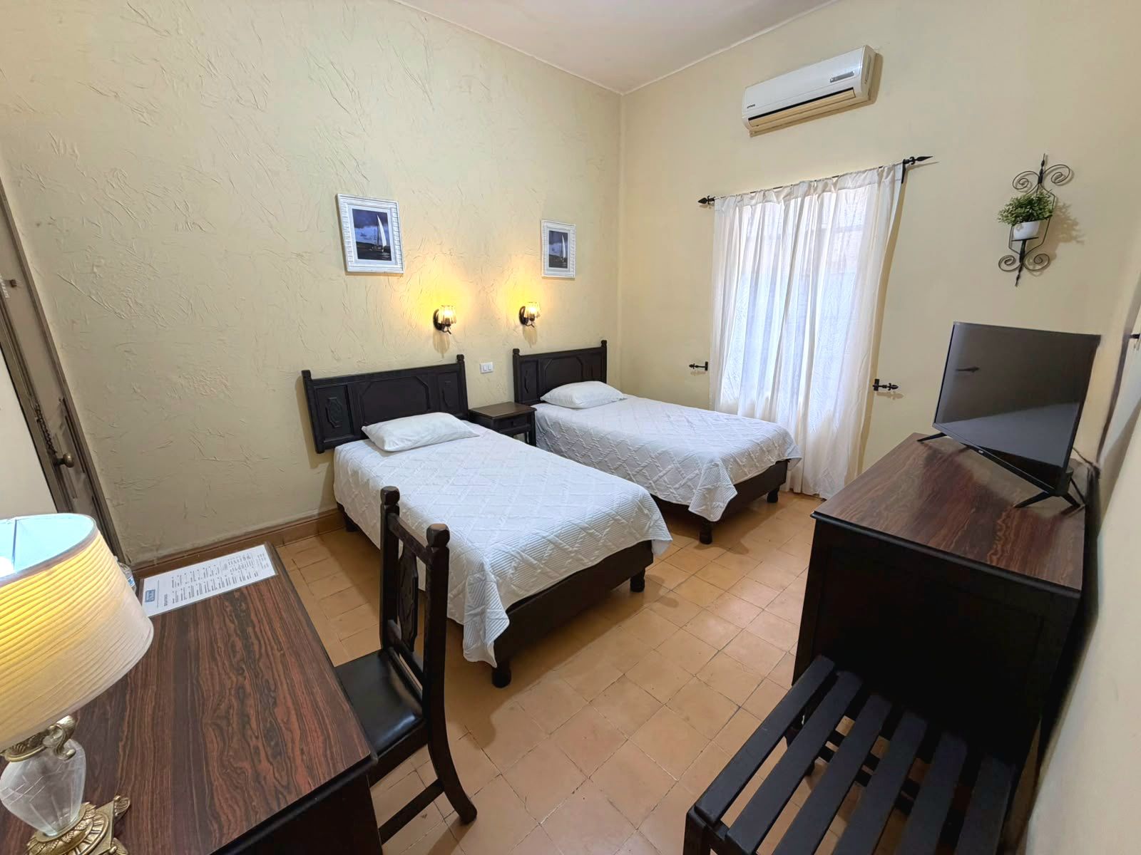 Habitación de hotel con dos camas, un escritorio con lámpara, televisión y aire acondicionado.