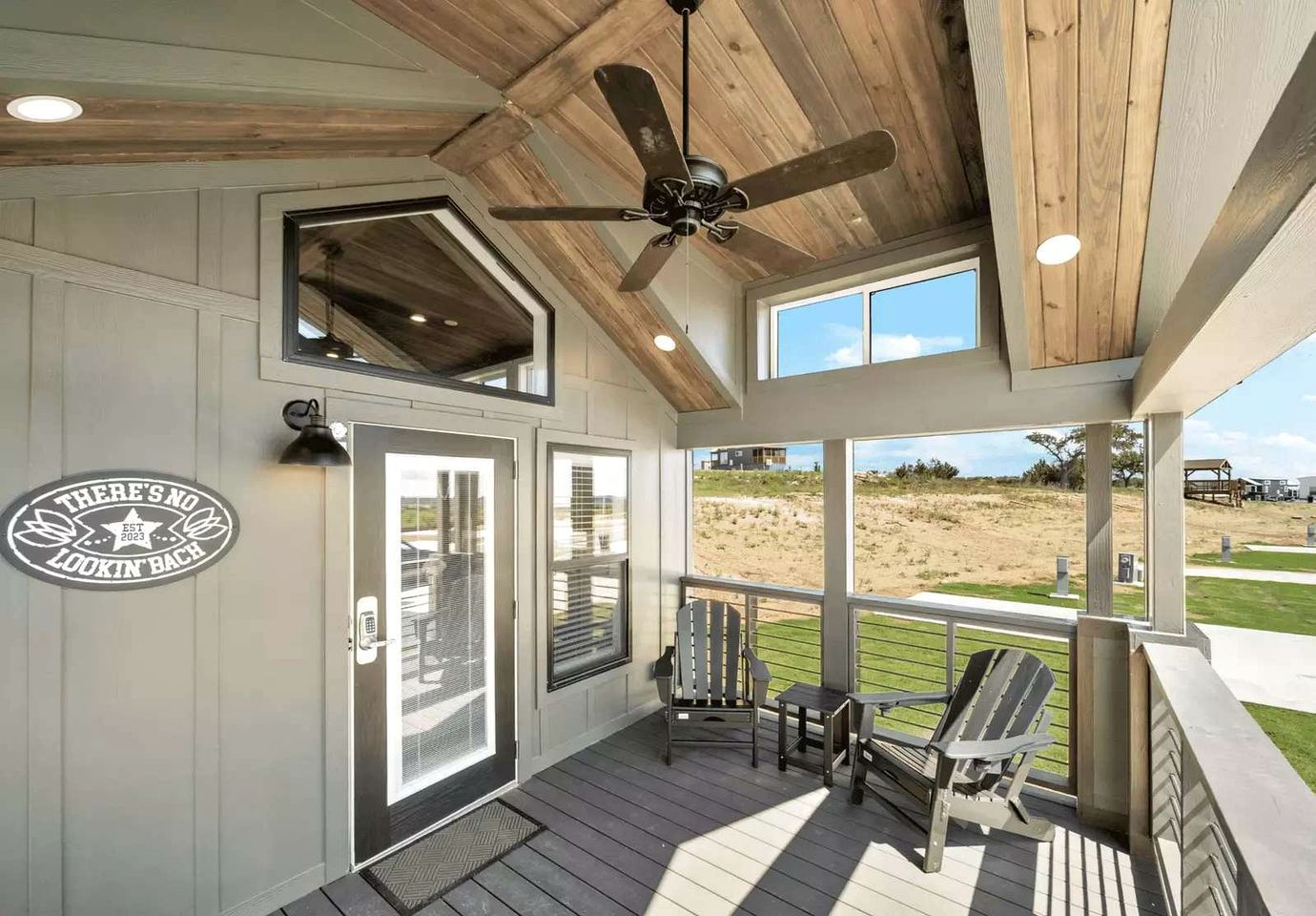 A covered porch with a ceiling fan, two doors with a view of the beach, and a sign on the wall.