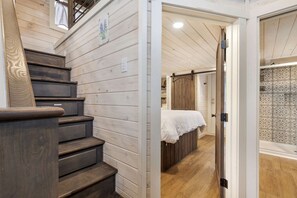 A wooden staircase leading to a bedroom with a bed and a bathroom with patterned tiles. - Refined Tiny Home Getaway with Resort Amenities Near Fredericksburg, TX (Fredericksburg)