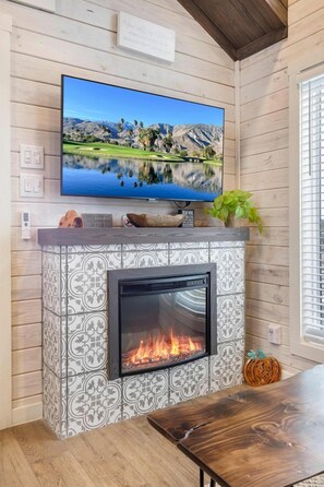 A fireplace with a TV mounted above it, a wooden table, and a plant on the mantel. - Refined Tiny Home Getaway with Resort Amenities Near Fredericksburg, TX (Fredericksburg)