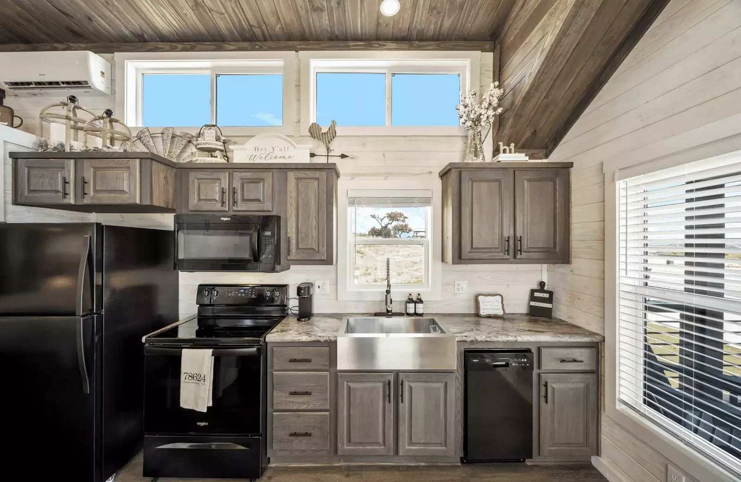 Cocina equipada con refrigerador de acero inoxidable, microondas, estufa y lavavajillas. Cuenta con gabinetes de madera y una ventana con vista al exterior.