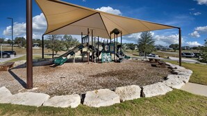 Un'area giochi con scivolo e strutture per arrampicata, circondata da una zona ombreggiata e un cordolo in pietra.