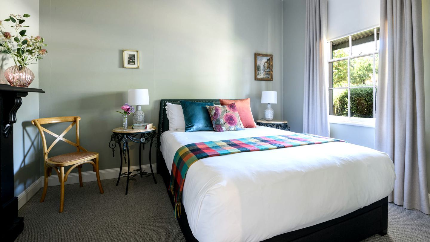 A neatly arranged bedroom with a bed, a chair, a small table, and a window with curtains.