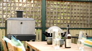 Un barbecue doté d’un écran numérique, une table avec une bouteille et des verres, et une clôture en bois en arrière-plan.