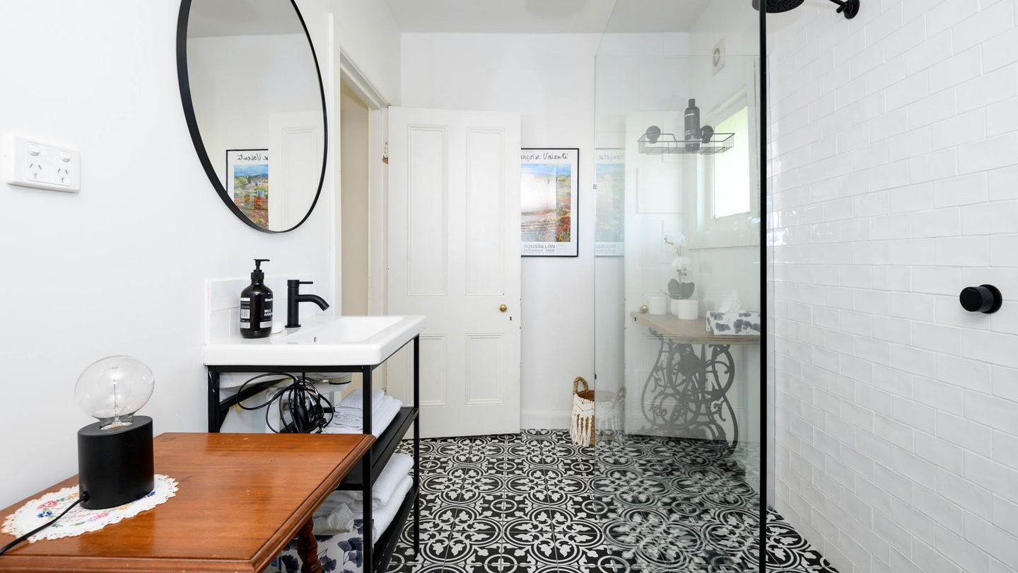 A bathroom with a white sink, a mirror, a black and white patterned floor, and a shower area with a glass door.
