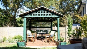 En træterrasse med en grøn pergola, to stole og et bord.