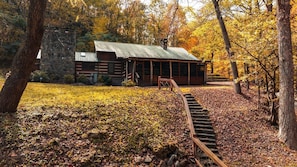 A rustic cabin with a stone foundation, wooden exterior, and a metal roof. A wooden staircase leads to the entrance. - Exclusive Retreat: Unique Cabin Getaway Along Norton Creek in Gatlinburg, TN (Gatlinburg)
