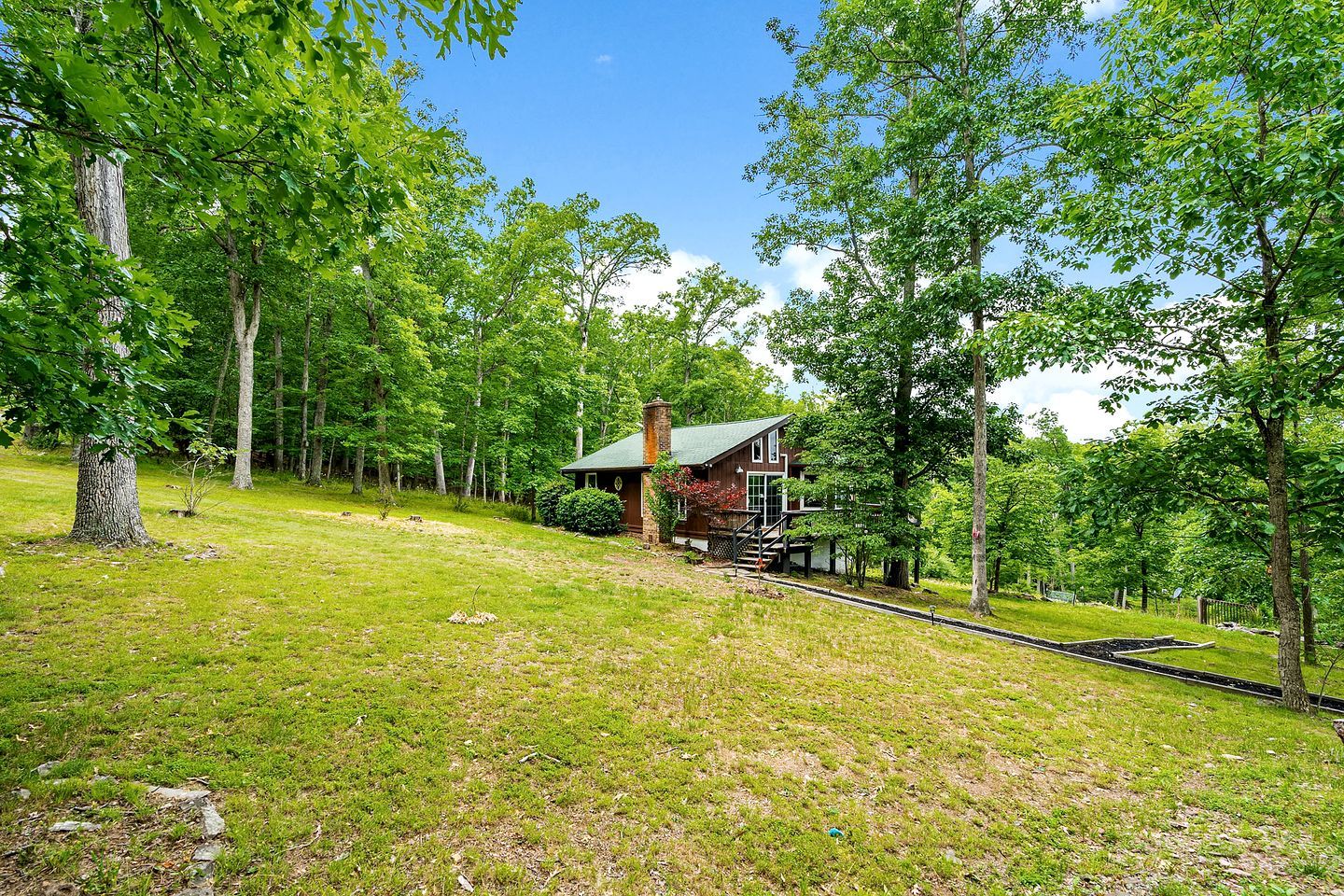 A cabin surrounded by trees with a grassy area in front.
