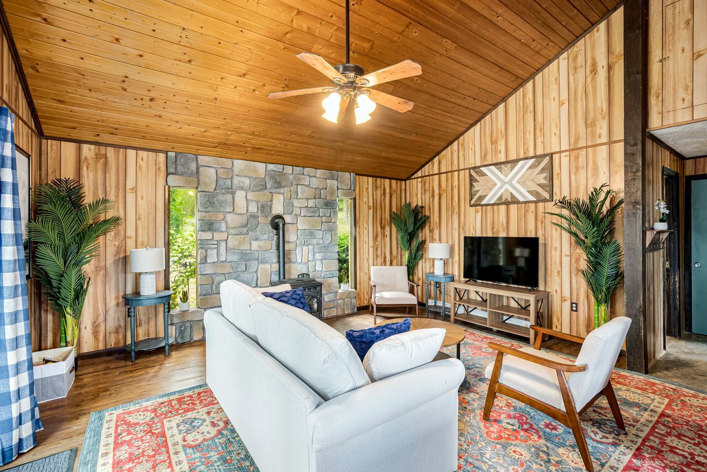 A cozy living room with a stone wall, wooden ceiling, and a large TV.