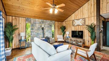 A cozy living room with a stone wall, wooden ceiling, and a large TV.