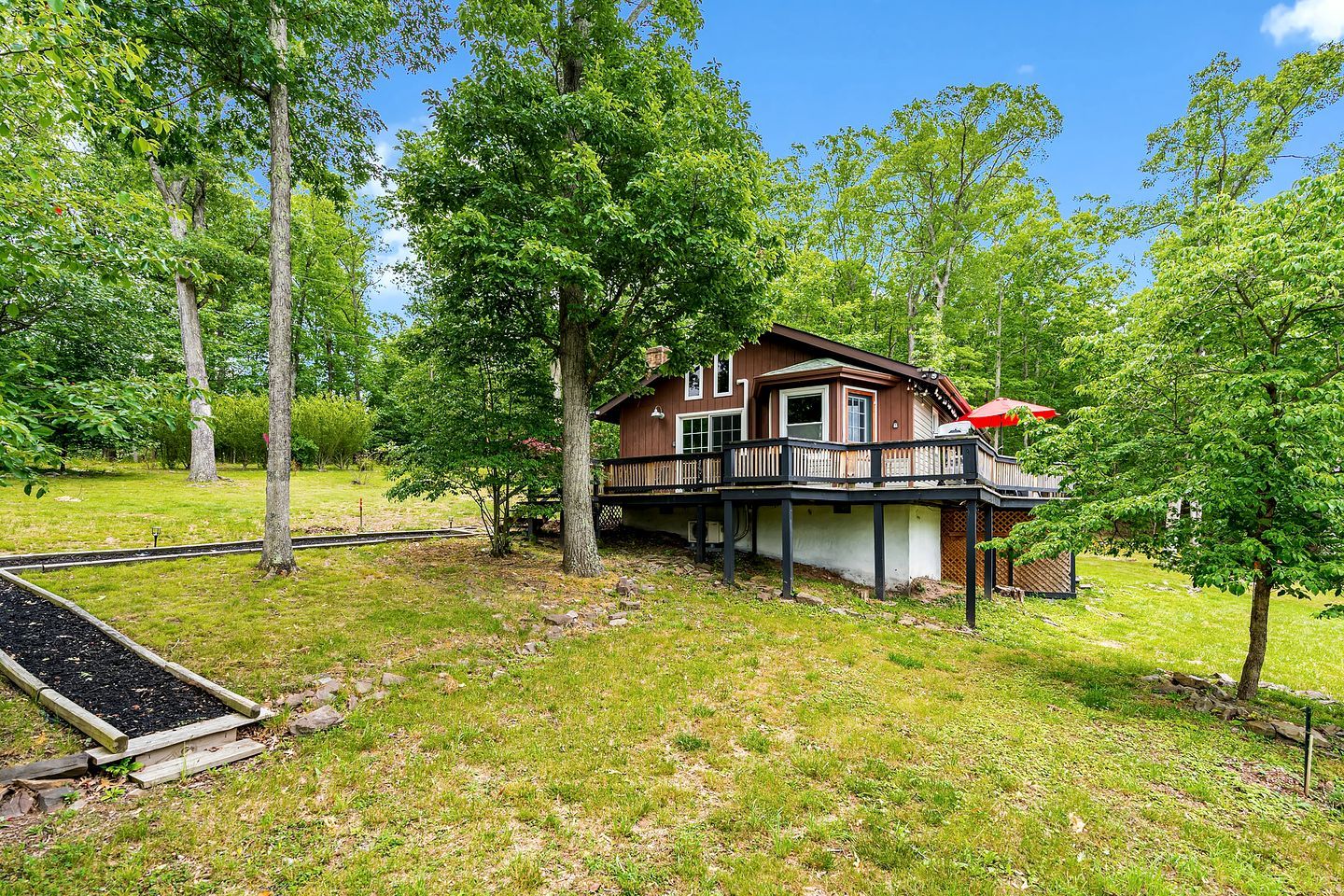 A wooden cabin with a deck, surrounded by trees and a grassy area.