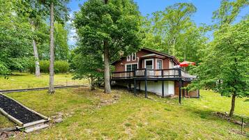 A wooden cabin with a deck, surrounded by trees and a grassy area.