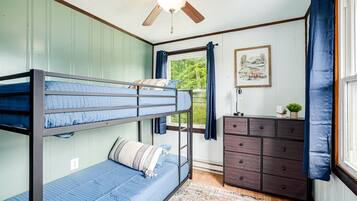 A bunk bed room with a ceiling fan, a dresser, a window with curtains, and a framed picture on the wall.