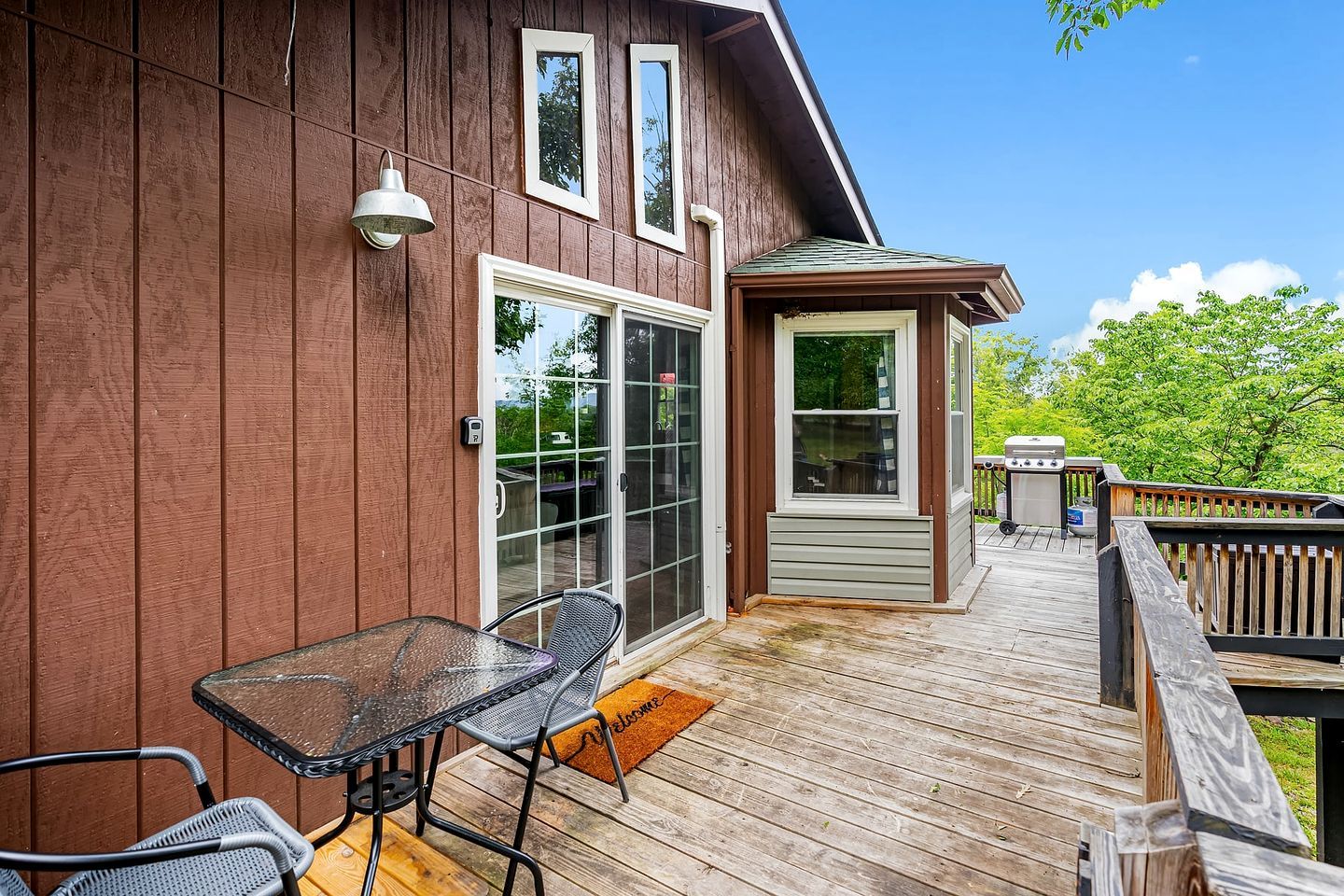 A wooden deck with a glass door entrance, a small table with chairs, and a barbecue grill.