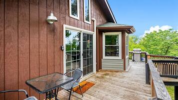 A wooden deck with a glass door entrance, a small table with chairs, and a barbecue grill.