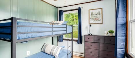 A bunk bed room with a ceiling fan, a dresser, a window with curtains, and a framed picture on the wall.