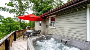 Un jacuzzi en una terraza de madera con una sombrilla roja, una mesa y sillas.