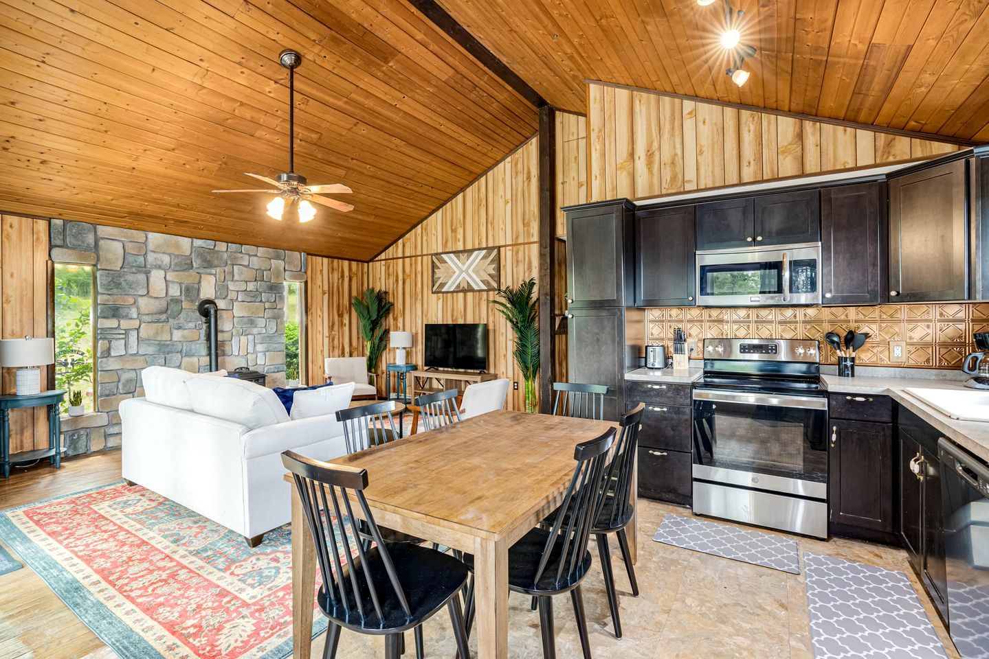 A modern kitchen with dark cabinets, stainless steel appliances, and a stone accent wall.