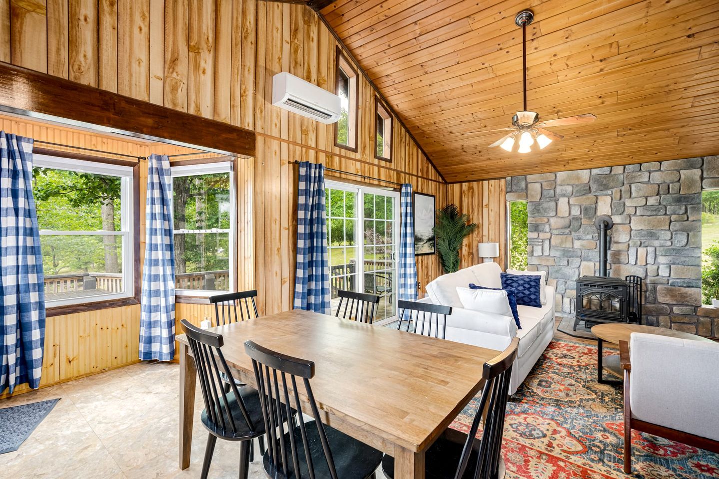 A wooden interior with a dining area, a stone fireplace, and a view of the outdoors.
