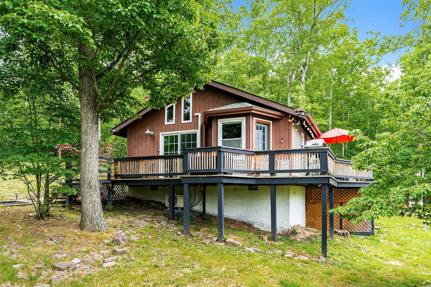 Une maison en bois à deux étages, dotée d’un balcon et entourée d’arbres.