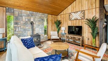 Ein gemütliches Wohnzimmer mit Steinwand, Holzvertäfelung, Kamin, Fernseher und bequemen Sitzmöglichkeiten.