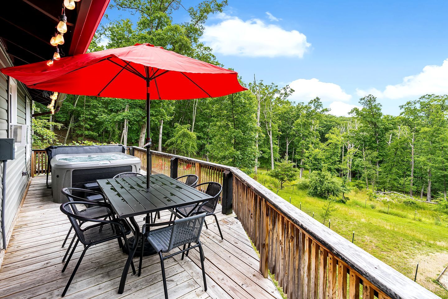 A wooden deck with a table and chairs, a red umbrella, and a hot tub.