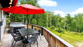 A wooden deck with a table and chairs, a red umbrella, and a hot tub.