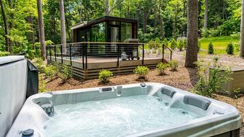 A hot tub in a forested area with a deck and a small cabin-like structure in the background.
