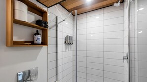 Eine Dusche mit Glastür, ein Holzregal mit Pflegeprodukten und ein Toilettenpapierhalter.
