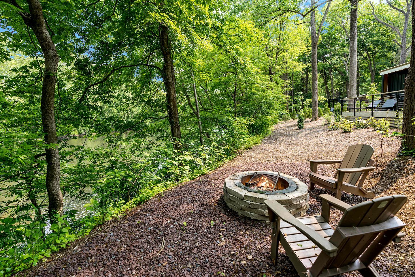 Ein runder Feuerkorb aus Stein mit zwei Adirondack-Stühlen und einem Kiesweg.