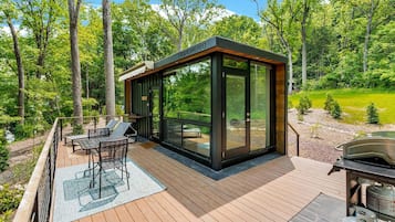 Eine moderne Terrassenausstattung im Freien mit einer verglasten Struktur, einem Grill und einem Essbereich.
