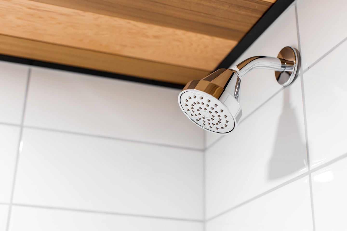A showerhead mounted on a white tiled wall with a wooden ceiling.