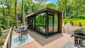 Eine moderne Terrassenausstattung im Freien mit einer verglasten Struktur, einem Grill und einem Essbereich.