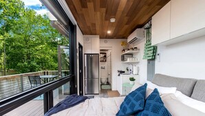 Ein modernes Schlafzimmer mit einem großen Bett, einem Balkon mit Blick auf Bäume und einer kleinen Küche im Hintergrund.