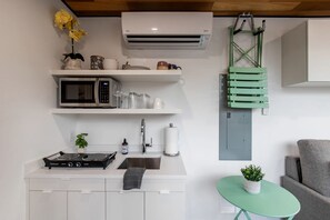 A modern kitchen with a microwave, stove, sink, and a small table with a plant. - Modern Riverside Container Home with Hot Tub and Fire Pit in Rileyville, VA (Rileyville)