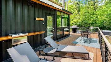 A modern outdoor deck with two lounge chairs, a wooden table, and a grill.