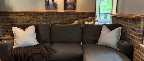 A modern living room with a sectional sofa, a patterned rug, and a brick accent wall.