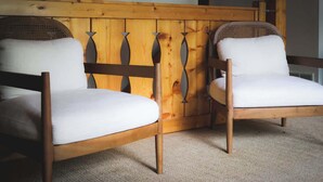 Duas cadeiras de madeira com almofadas brancas, encosto de fibra trançada e cabeceira de madeira com design exclusivo.