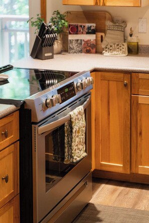 A kitchen with a stainless steel stove, wooden cabinets, and a window with a view. - Waterfront Lake Views w/ Hot tub in Hocking Hills (Logan)