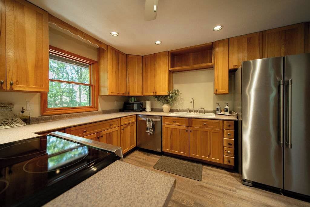 Een moderne keuken met houten kasten, roestvrijstalen apparatuur en een raam dat voor natuurlijk licht zorgt.