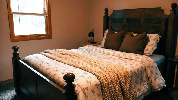 Um quarto com cama de madeira, mesa de cabeceira, luminária e janela com persianas.