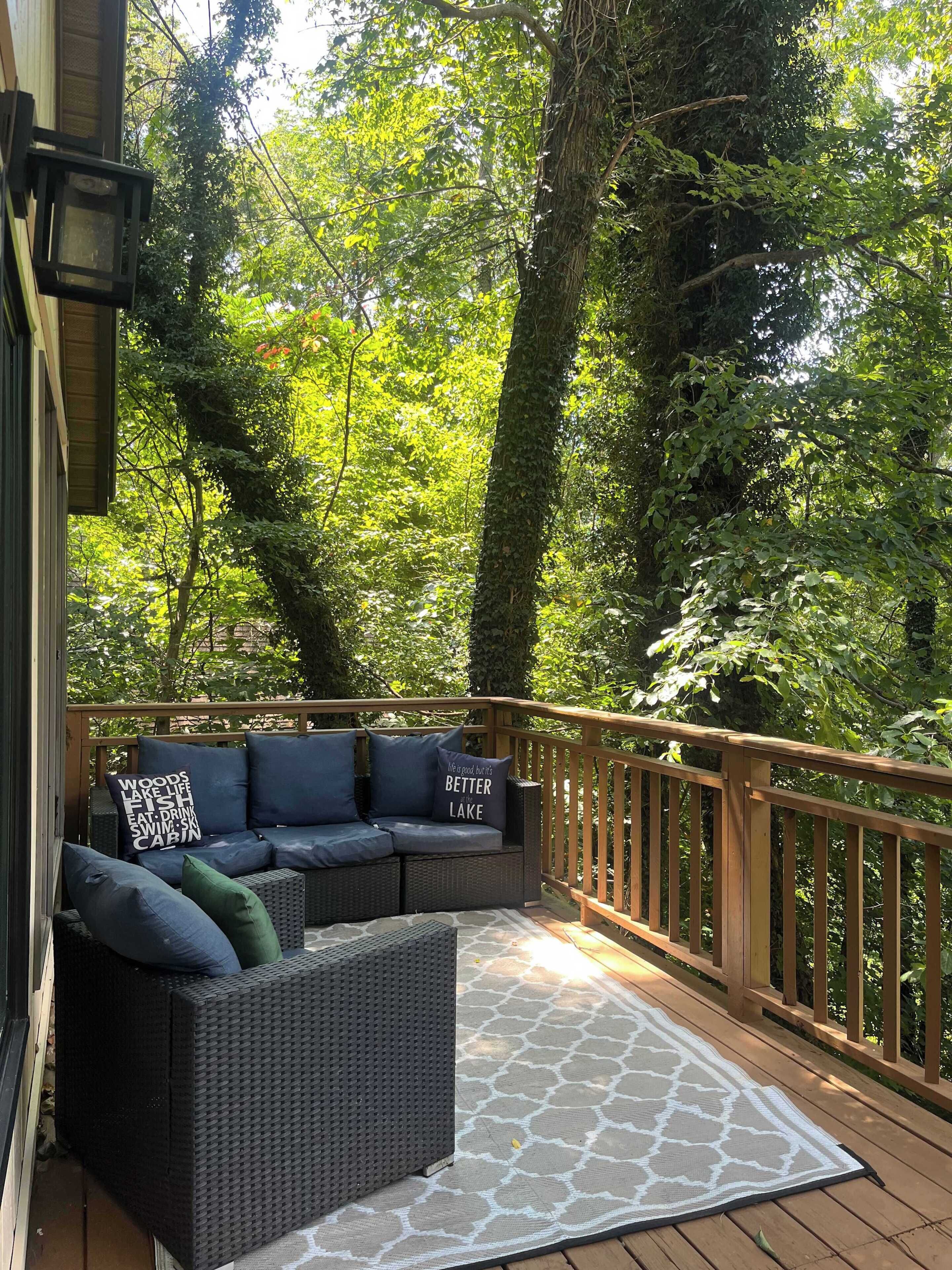 Une terrasse en bois agrémentée d’un canapé en osier et de coussins, le tout entouré d’une végétation luxuriante.