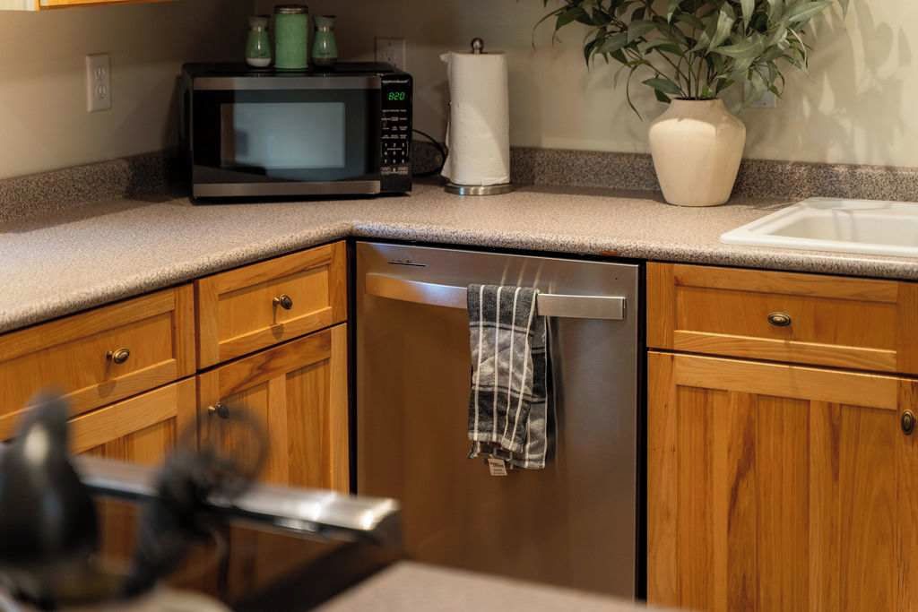 A kitchen with wooden cabinets, a microwave, a dishwashing machine, and a potted plant.